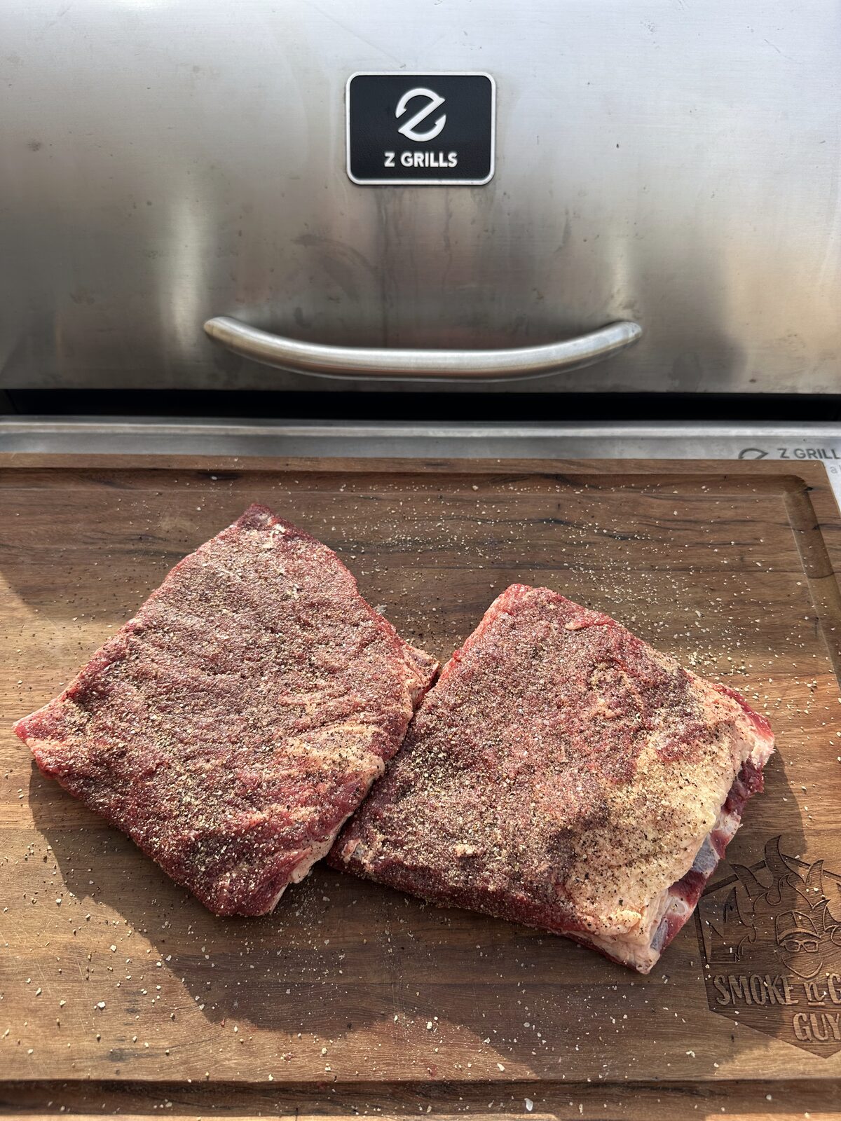 Seasoned beef short ribs on a board in front of a Z Grills pellet smoker